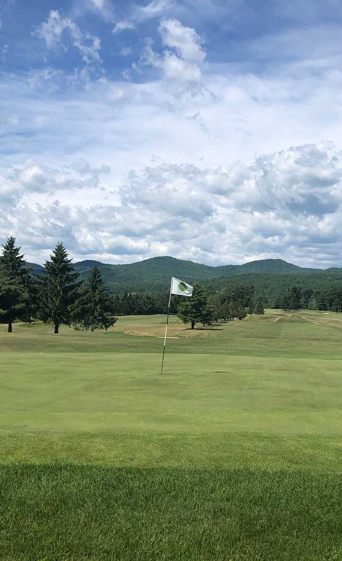 Adirondack golf course with flag on tee with mountains in background